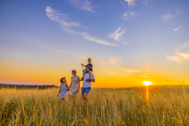 istock Happy family walking while exploring in grassy field during sunset 1414490494