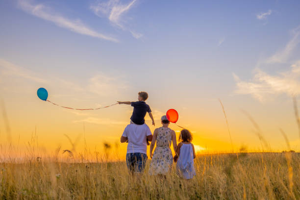 parents et enfants marchant tout en explorant dans la prairie contre le ciel - sun sky child balloon photos et images de collection