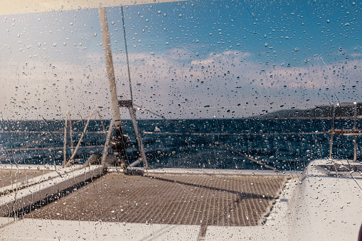 Cropped image view of boat deck against sky seen from wet glass window