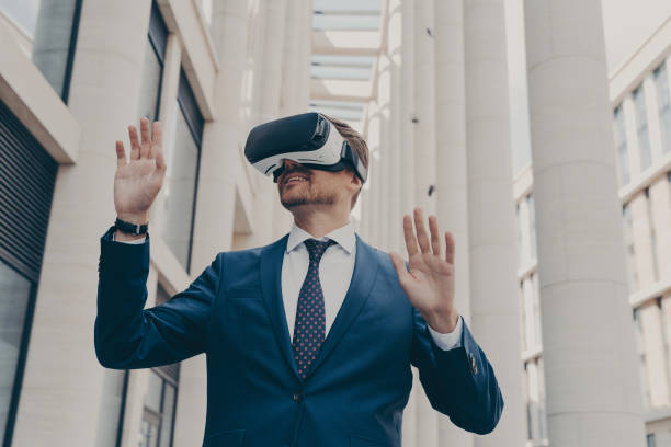istock Man in formal blue suit walking around in virtual reality while wearing VR goggles 1414492522