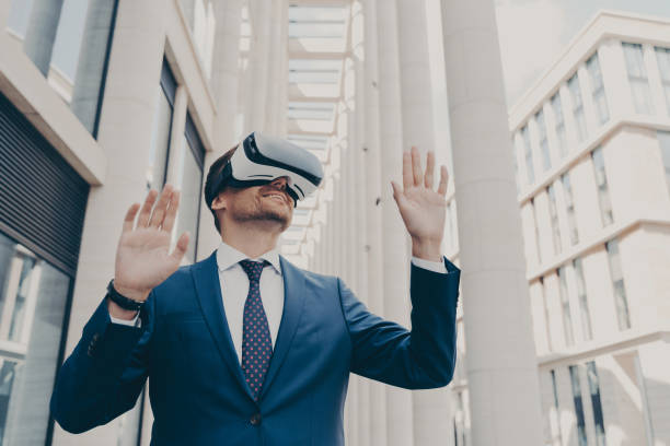 istock Young modern businessman in VR goggles on head working in augmented reality world and smiling 1414492531