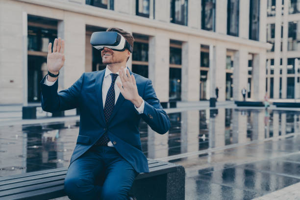 istock Man in VR goggles trying to reach something in virtual reality with his hands while sitting outdoors 1414492541