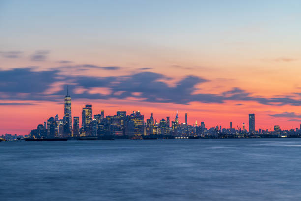 Manhattan skyline and the Hudson River (Upper New York Bay) in the foreground. Very early morning, right before sunrise. Dramatic magenta and orange sky with violet clouts. July 13, 2022. NYC. Brooklyn. Bay Ridge. New York. USA