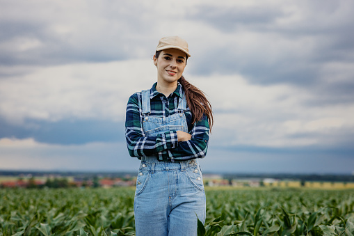 Portrait of smiling young farmer standing with arms crossed amidst crops in corn field