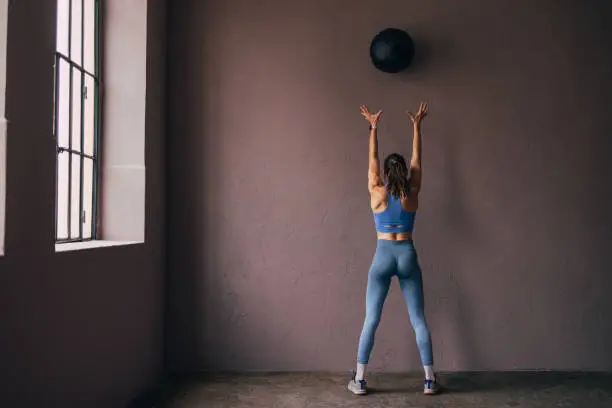 Back shot of a Caucasian woman in sportswear doing her workout with a medicine ball in the gym.