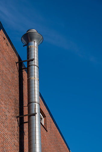 a silver-colored exhaust pipe on a house wall in front of a blue sky