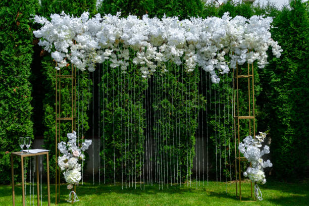 White wedding arch on a background of evergreen thuja. Summer wedding ceremony in the park stock photo