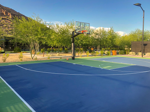 Mountain side blue and green outdoor basketball court with ball.
