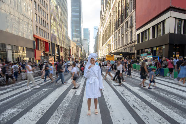 mujer en bata de baño con taza de café se queda en el cruce de peatones con personas que pasan en el fondo. foto conceptual. tómate tu tiempo y deja que el mundo se mueva. - bathrobe women cup towel fotografías e imágenes de stock