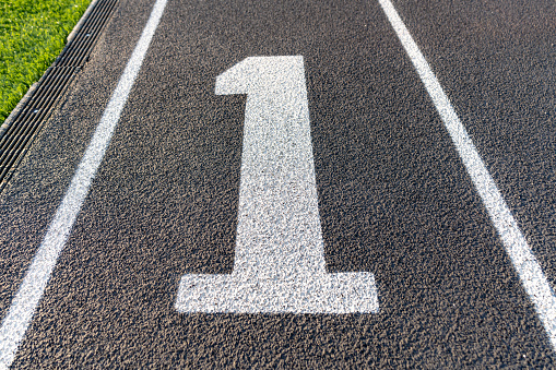 Close up lane number one, 1, on a new black running track with white lane lines and other markings.