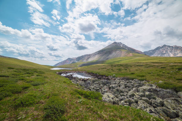 istock Scenic alpine landscape with two mountain lakes in sunlit mountain valley under cloudy sky. Dramatic sunny scenery with clouds reflection in water mirror of small lake among lichen stones in sunlight. 1414520729