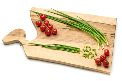 Bunches of fresh red cherry tomatoes and young green onion on cutting board isolated on white background. Ripe tomatoes on green stems. Bunch of fresh onion. Fresh organic vitamin vegetables.