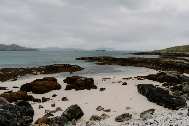 Gurteen Bay at sunset shows a quiet, sandy beach stretching along the clear Atlantic waters. The scene captures the natural beauty of the Irish coast, with gentle waves and an overcast sky