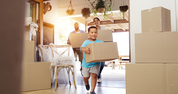 Happy family moving into new home and cheerful or excited child son and parents carrying boxes into their house. First time home owners looking satisfied with real estate property while settling in