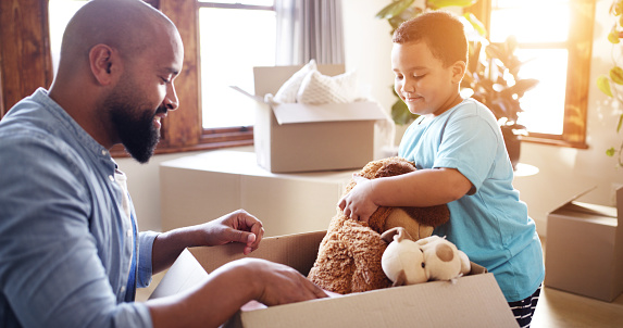 Family packing boxes while moving into a new house, unpacking after a move and bonding after relocation. Father and son putting toys into a box after buying an apartment, adoption or foster care