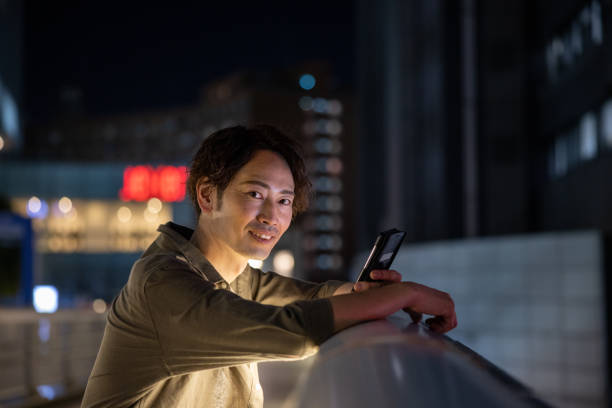 Portrait of man using smart phone on pedestrian bridge at night