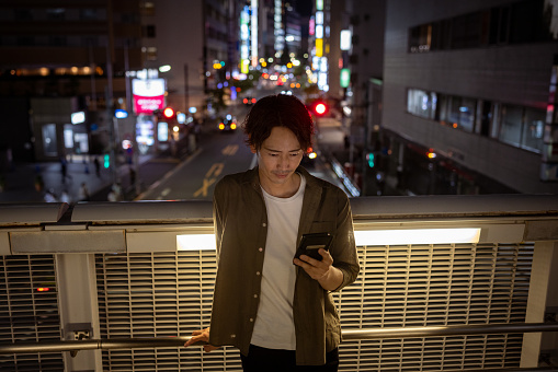 Japanese man using smart phone on pedestrian bridge at night