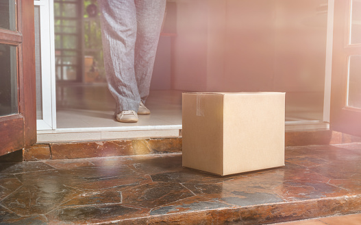 Woman picking up a cardboard box at the doorstep of a delivery