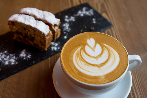 A large cup of cappuccino (lotus latte art pattern), with two slices of muffin under powdered sugar on a slate, a very tasty break