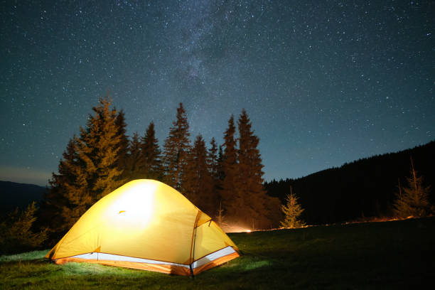 istock Bright illuminated tourist tent glowing on camping site in dark mountains under night sky with sparkling stars. Active lifestyle concept. 1414546478