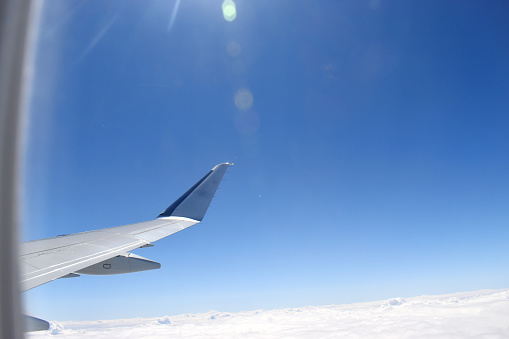 Airplane wing flying in the atmosphere with horizon blue sky above beautiful white clouds.