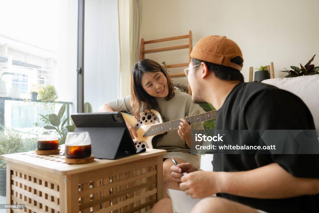 Young Asian couple practicing guitar in living room Young Asian couple happily practicing guitar through online lessons together in the living room Couple - Relationship Stock Photo