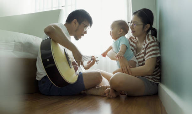 padre asiatico che suona la chitarra con il ragazzo e la madre - toddler music asian ethnicity child foto e immagini stock