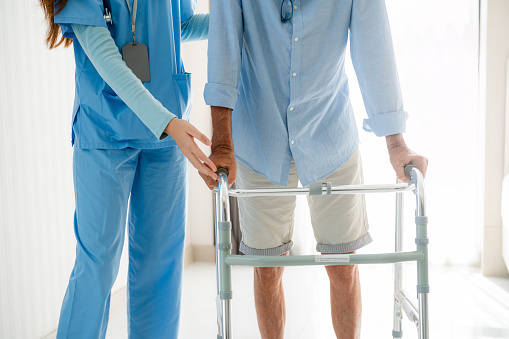 Closeup of nurse helping elderly man get out of bed and walk around the room.