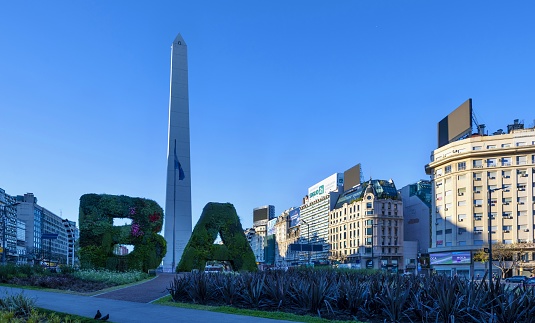 Buenos Aires, Argentina, October 31, 2019: A car passes the Obelisco de Buenos Aires at sunrise. The obelisk is a national historic monument and icon of the city, in the morning sunlight. It was erected in 1936 to commemorate the quadricentennial of the first foundation of the city.