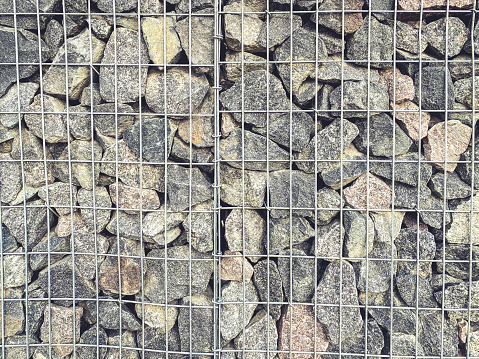 texture, background. large, gray stones lie behind a high metal fence. stones for decorative finishing of the building, construction of columns