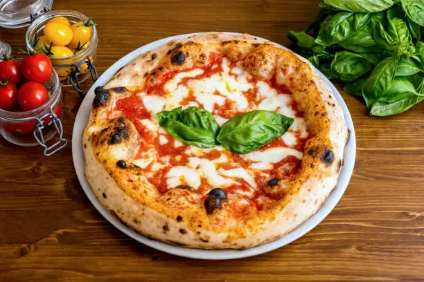 A delicious and tasty Italian pizza Margherita with fresh tomatoes, buffalo mozzarella and extra virgin olive oil, strictly cooked in a wood oven, according to the original tradition of Naples. In 2017 the art of Neapolitan pizza was declared by UNESCO as an Intangible Cultural Heritage. Image in High Definition format.