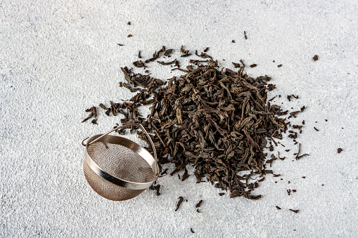 tea strainer and a pile of dried tea leaves on a gray background, selective focus