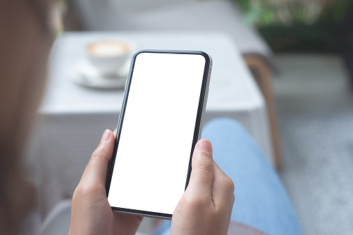 Cell phone mockup image blank white screen. Woman hand holding texting using mobile phone at coffee shop. Background and copy space for advertisement