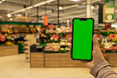 Mobile phone Chroma key for mobile app application. Close up of woman hand holds smart phone with green screen at shopping mall store. Sale Economy Buying food at supermarket, grocery shop center online. Gadgets Advertisement template mock up