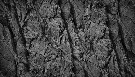 Black white rock texture background. Rough mountain surface with cracks. Close-up. Dark gray stone basalt background for design.