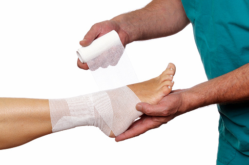 Close-up of male doctor bandaging foot of female patient.