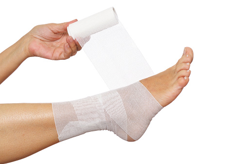 Close-up of mature woman with sprained ankle applying medical bandage.