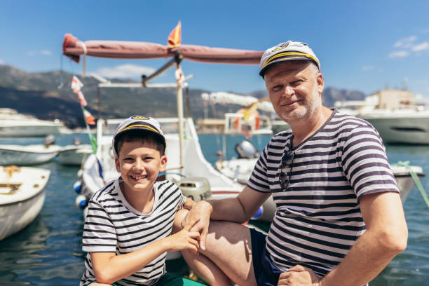 Father and son spending time at marina on summer day. They are dressed in sailor shirts and caps.