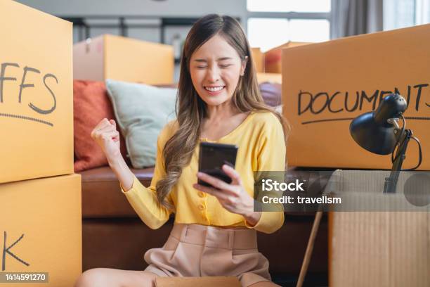 Asian Mature Adult Female Woman Is Packing And Unpacking As She Is Moving Into A New Place House She Is Using Her Smartphone To Talk And Chat Text To Friends And Family Or Finding A Delivery Service Nearbyhome Moving Ideas Concept Stock Photo - Download Image Now