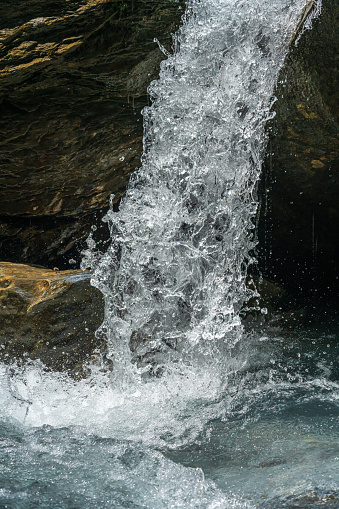 Falling jet of water from a mountain stream in front of a rock. With very short exposure, the splashing water appears like a frozen water column.