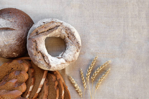 pane cotto. pagnotta di pane. prodotti da forno freschi su tavola di legno. concetto di cibo sano. vista dall'alto. posa piatta. fette di pane a lievitazione naturale fatto in casa con farina su fondo di lino rustico. spighe di grano - field brown text harvesting foto e immagini stock