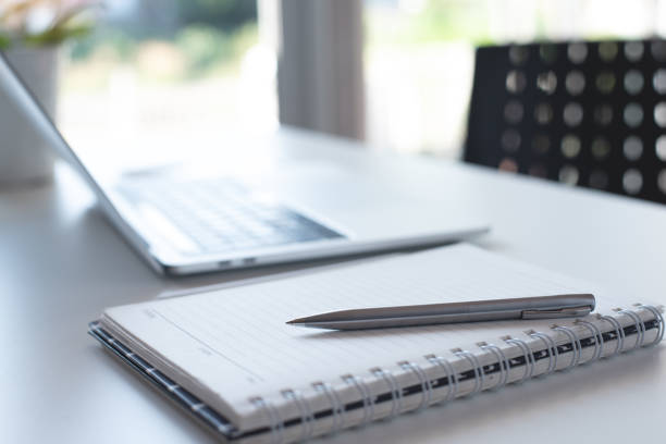 Pen, paper notebook and laptop computer on white office table with no people, blurred for business background