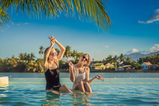 dos hermosas mujeres jóvenes sentadas junto a la piscina de un complejo durante las vacaciones de verano. fiesta, turismo en países tropicales - vitamin d fun friendship healthy eating fotografías e imágenes de stock