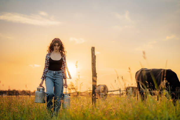 istock Young woman holding milk canisters while walking in field 1414600384