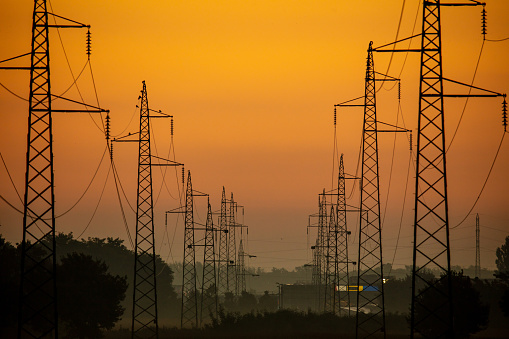 High voltage power poles in agricultural field against sky during sunrise