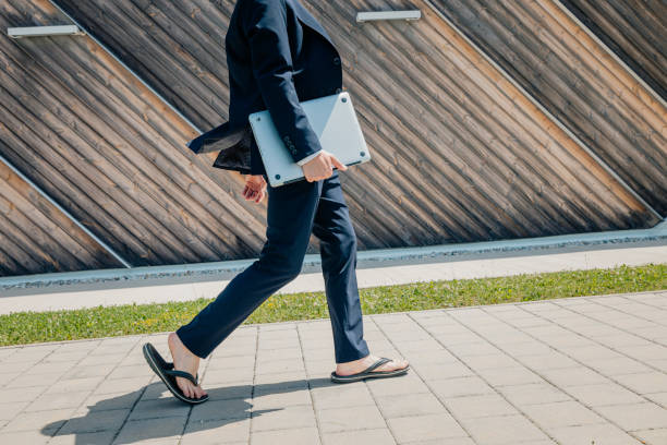 istock Businessman wearing suit walking with laptop on footpath by wall 1414602529