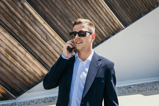 Confident politician talking on mobile phone while standing against wall during sunny day