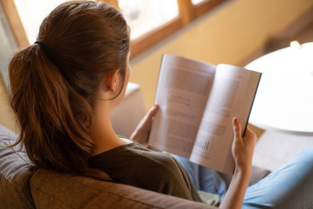 istock girl with ponytail reading book on her sofa 1414602610