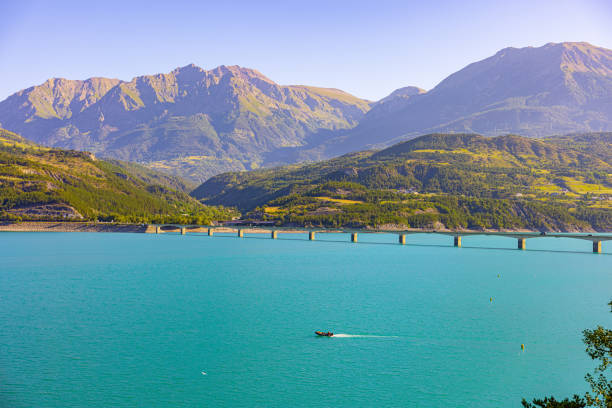 Distant boat moving by bridge over beautiful lake against mountain range during sunny day