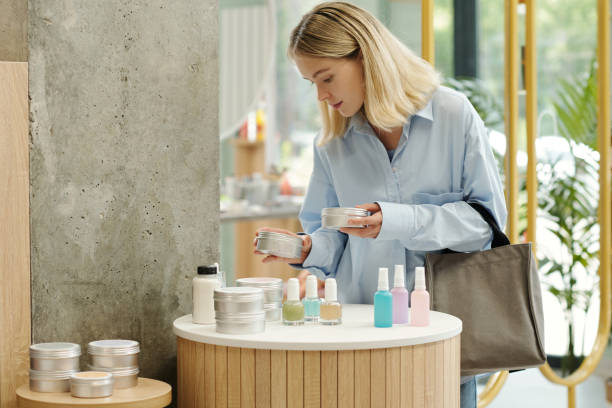 Young blond woman choosing body cream or scrub in tin jar in supermarket stock photo